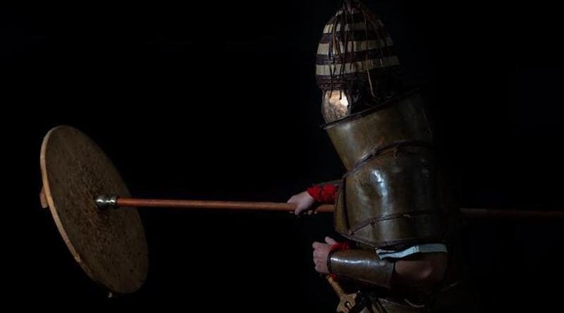 Man wearing replica armour and hitting a sheild with a spear/staff. CREDIT: Andreas Flouris and Marija Marković.