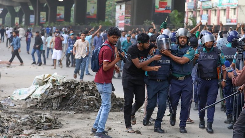 Policemen escort a colleague to safety after he was struck by a brick during a clash between pro-and anti-quota protesters, Dhaka, July 15, 2024. [Minhaz Uddin/BenarNews]